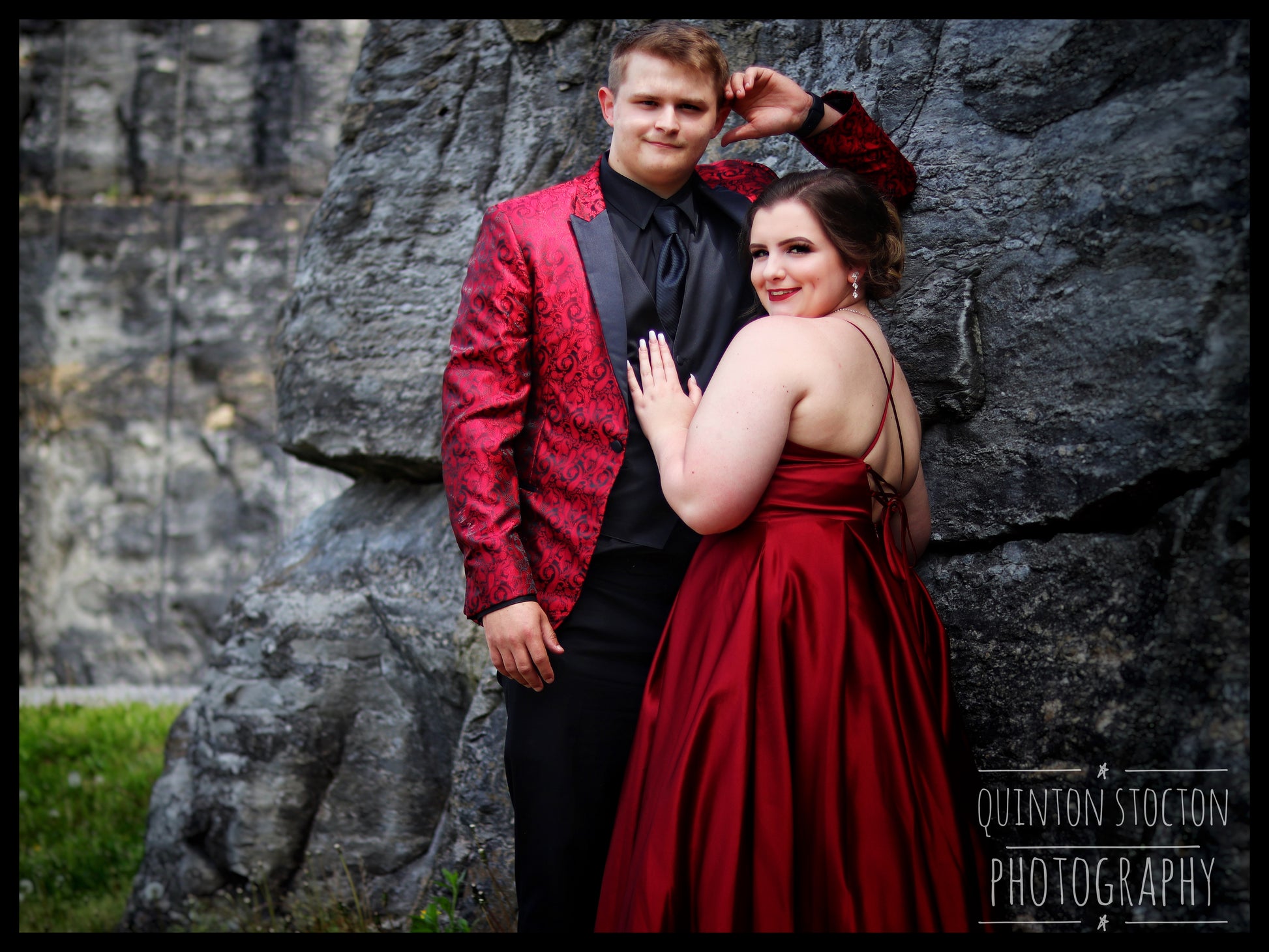 Event photography: Couple posing for prom pictures, dressed in red formal wear against a stone backdrop.