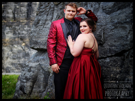 Event photography: Couple posing for prom pictures, dressed in red formal wear against a stone backdrop.