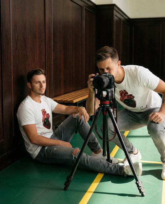 Two identical men with a camera and tripod in a room with wooden paneling.