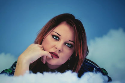 Woman with red hair lying on a snowy surface with string lights, against a blue sky.